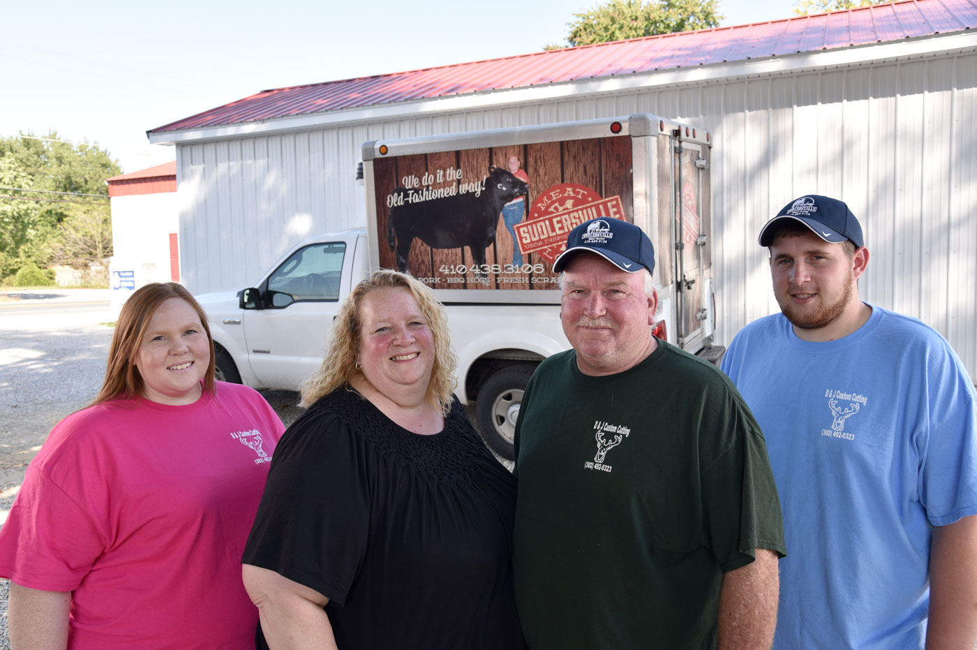 Dwayne, Dawna, and their son in front of the Sudlersville Meat Locker truck with the red barn building behind them